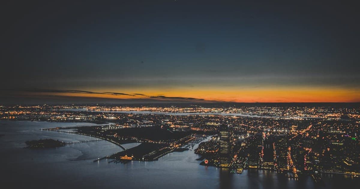Aerial view of New York City skyline at twilight with glowing city lights and a vibrant sunset.