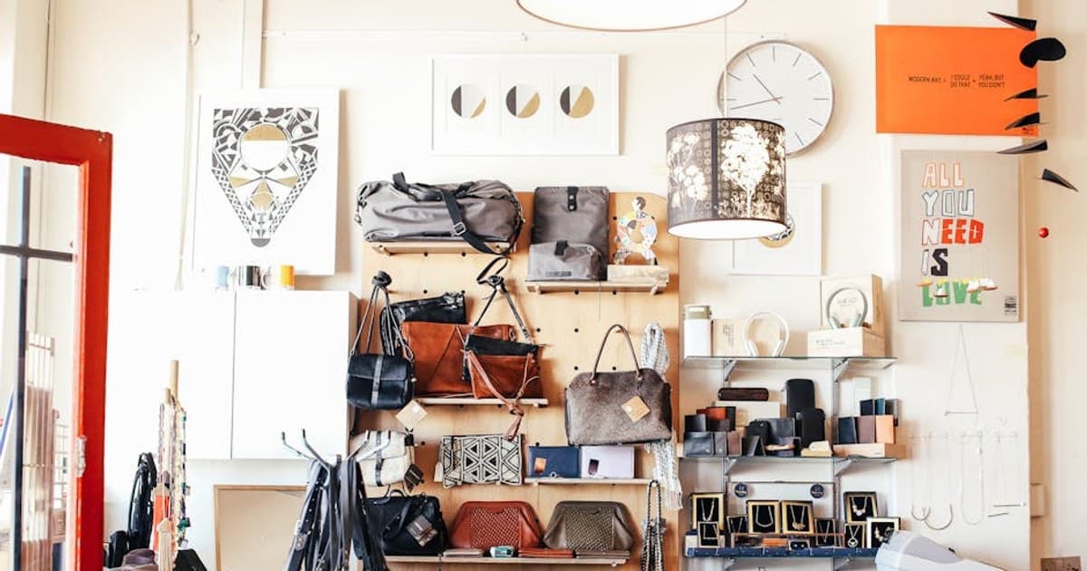 Abundance of stylish bags placed on shelves near wall with various goods and decorations in modern light shop with cashbox