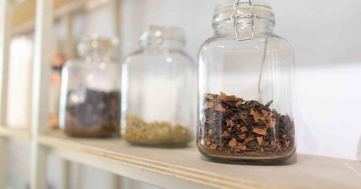 Close-up of glass jars filled with dried herbs on a wooden kitchen shelf.
