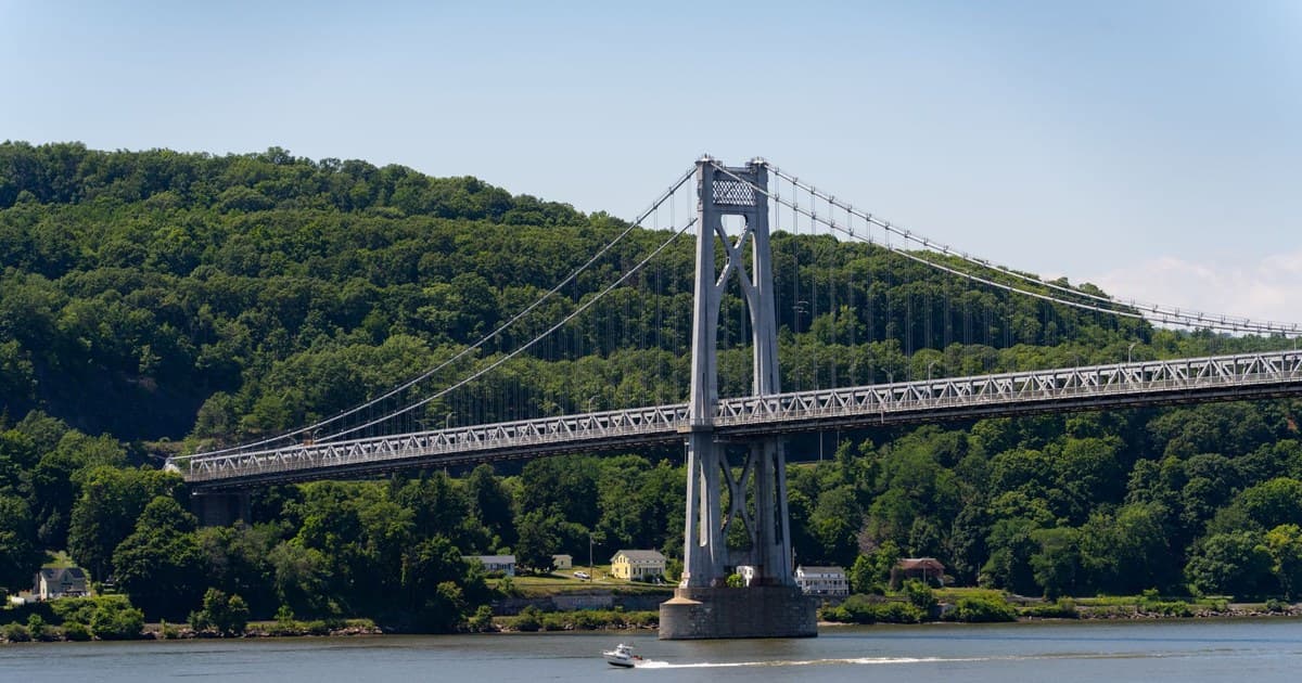 A serene daytime view of the Mid-Hudson Bridge spanning over the river with lush green forests in the background.