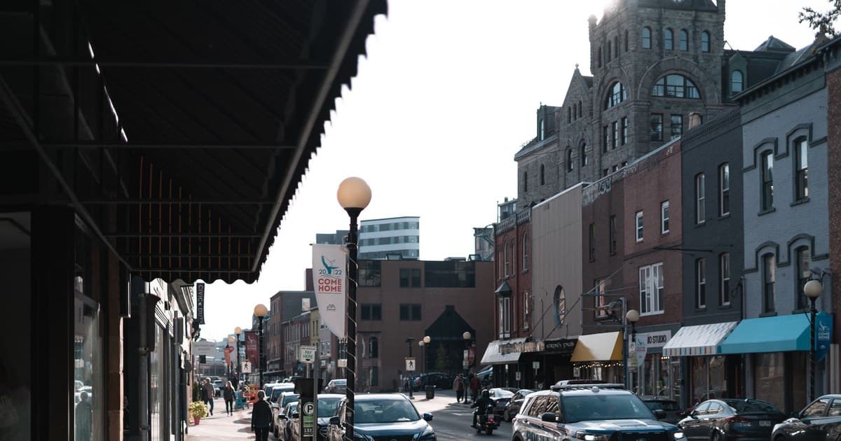 Lively urban street scene with parked cars and pedestrians in front of historic buildings.