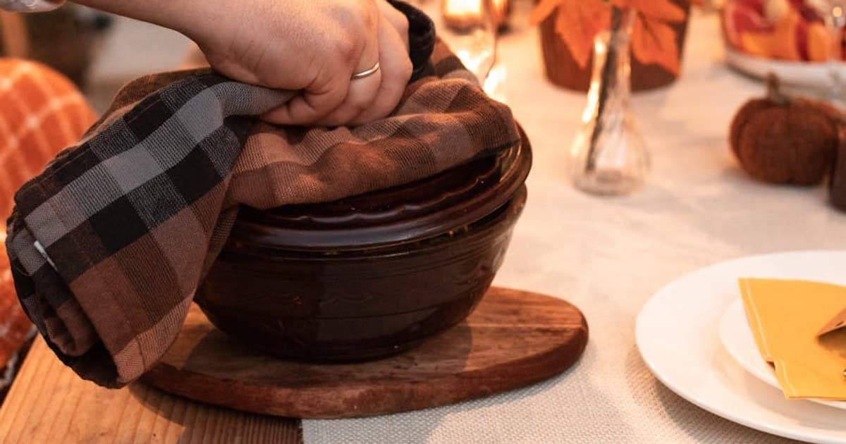 A warm, inviting autumn dinner setting with a hand lifting the lid from a ceramic dish.