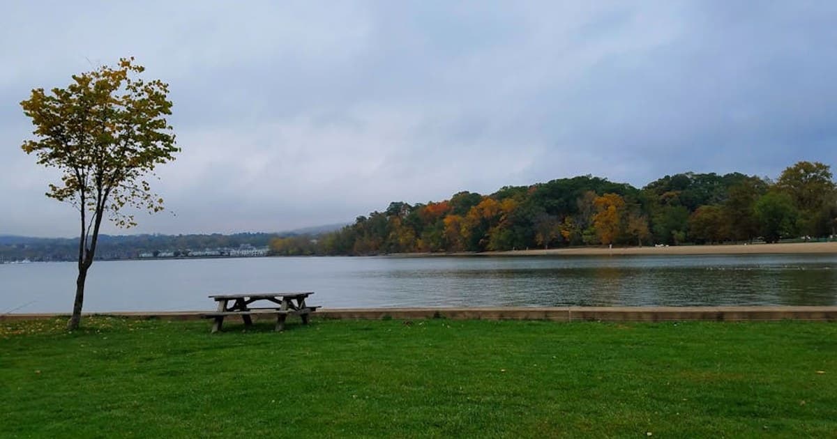 Peaceful park scene with fall foliage, calm waters, and a picnic table.