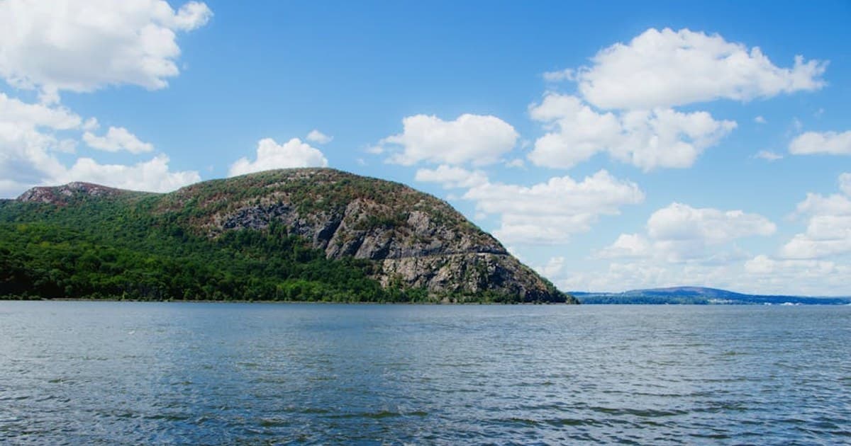 Beautiful landscape of Bear Mountain reflected in the Hudson River under a clear blue sky.