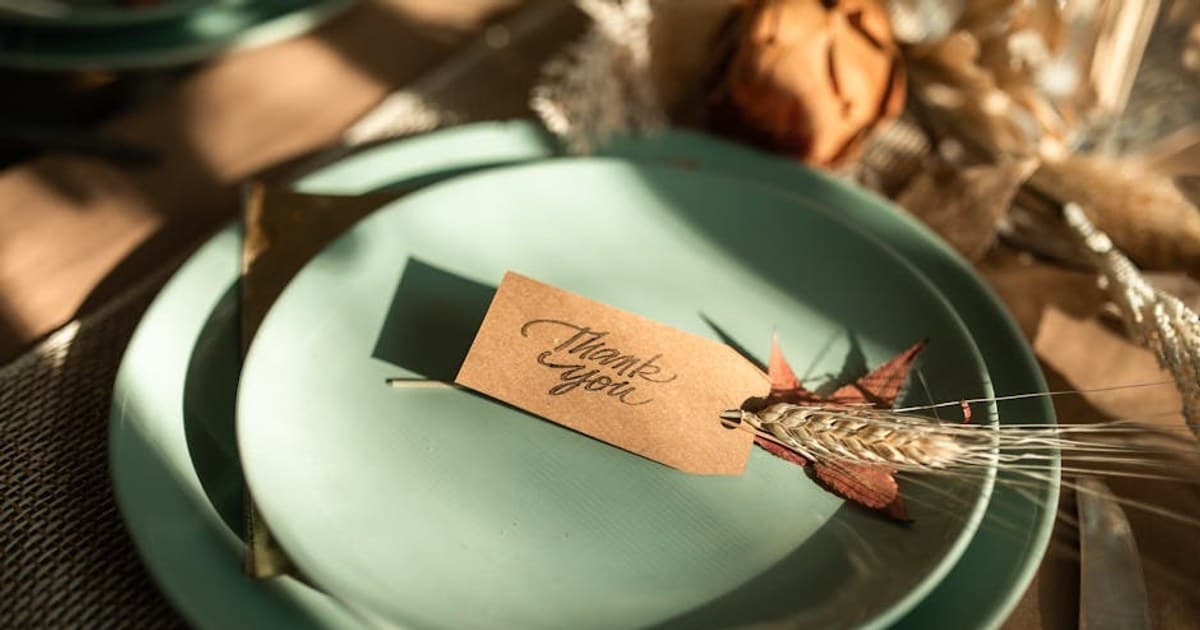 A sophisticated Thanksgiving table setup featuring a 'Thank You' card on mellow green plates, perfect for seasonal celebrations.
