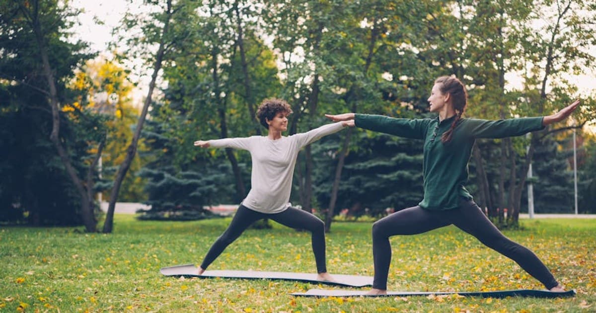 Two women practicing yoga outdoors on mats in a park during fall.