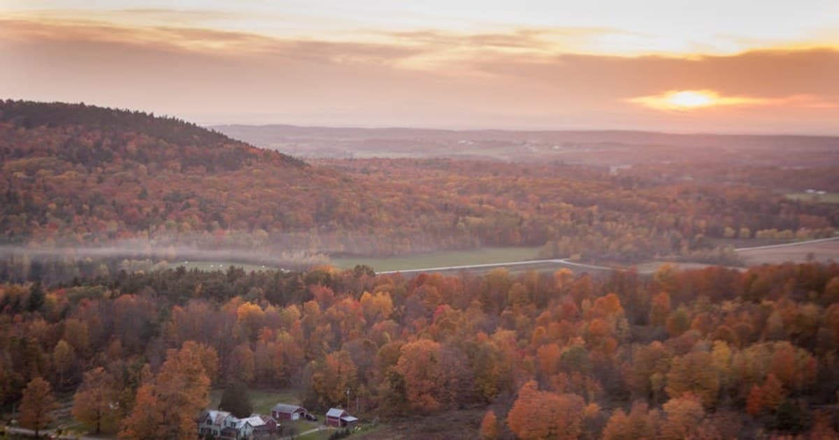 Aerial view of a picturesque countryside with autumn foliage and farmhouses at sunset.