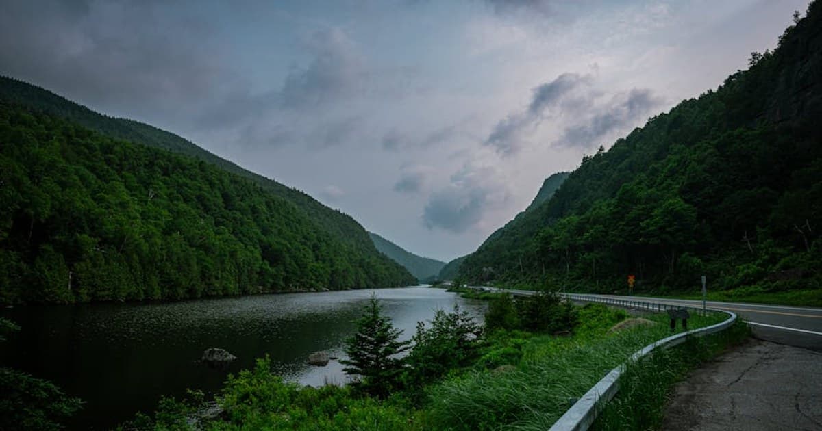 Lush green valley with river, mountains, and a scenic road curve.