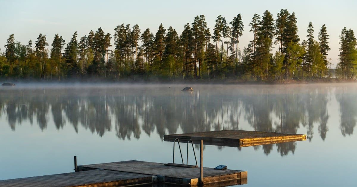 Tranquil misty lake scenery with reflections and wooden docks at dawn.