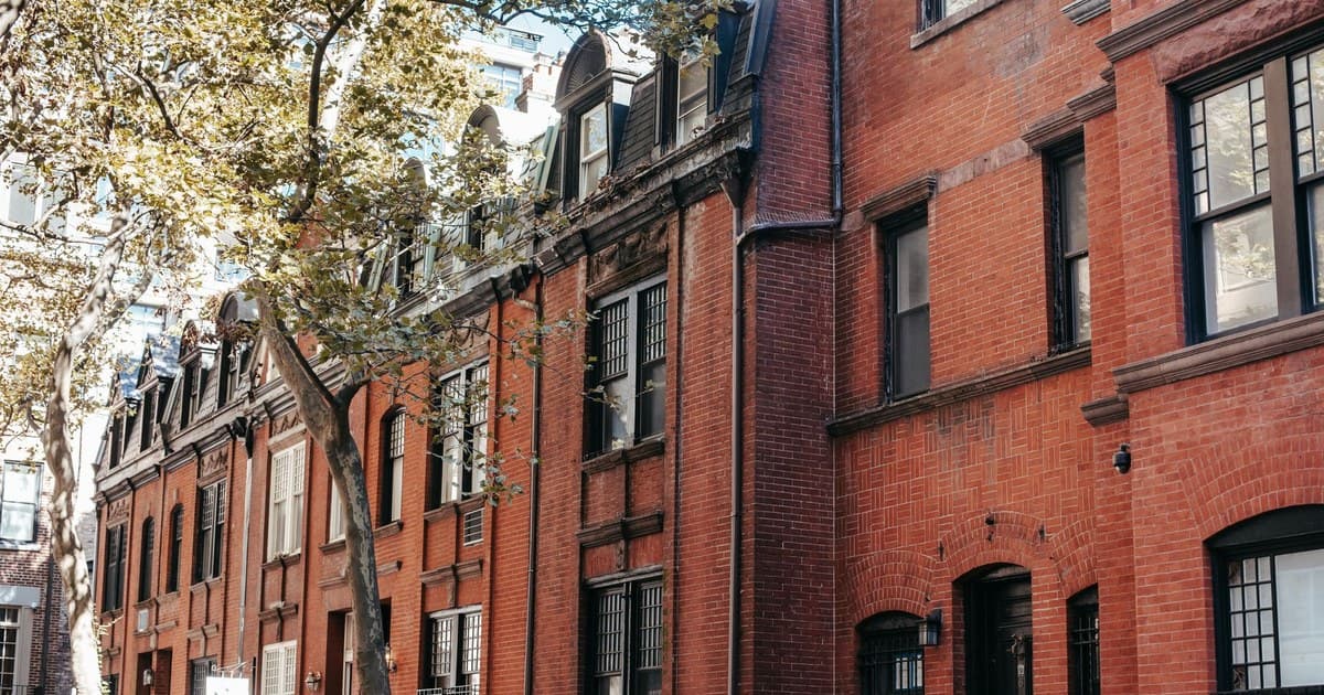 Exterior of aged brick residential building with windows and stairs located on city street on sunny autumn day